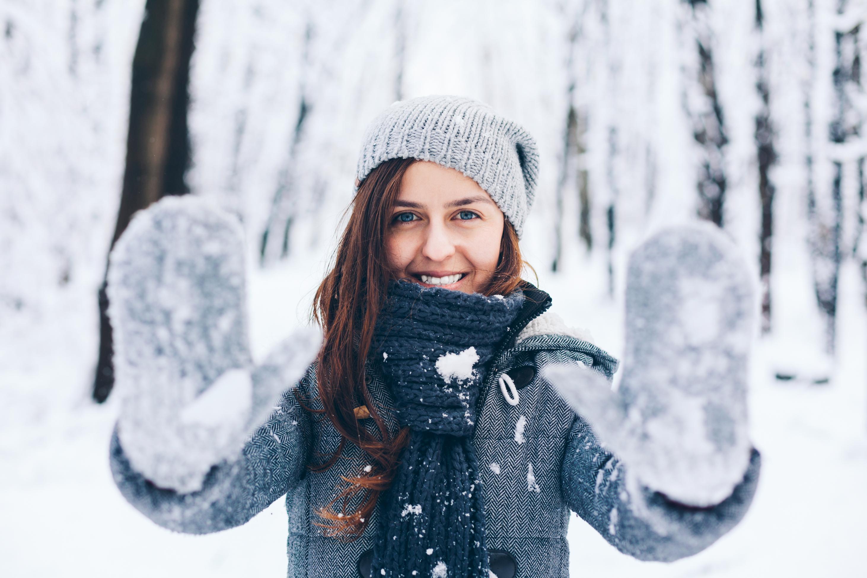 Mujer con gorro y guantes jugando con la nieve
