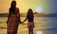 Mujer y niña en la playa mirando puesta de sol