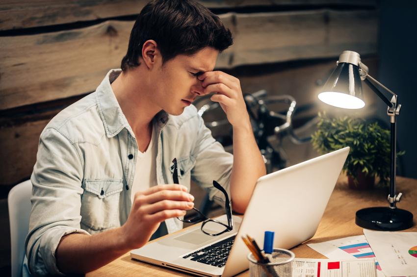 Hombre joven se quita las gafas mientras trabaja en el ordenador y se frota los ojos
