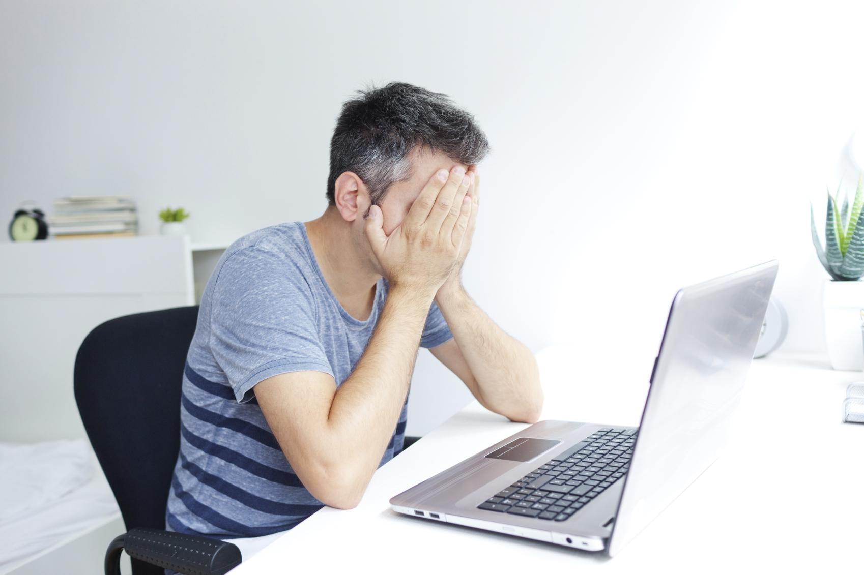 Hombre tapándose la cara mientras trabaja con un ordenador portátil