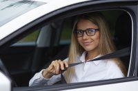 Mujer con gafas y camisa blanca poniéndose el cinturón del coche