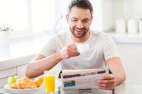 Hombre desayunando y leyendo un periódico