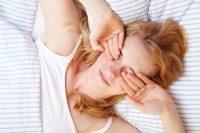 Mujer rubia se frota los ojos en la cama