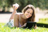 Mujer sonrie mientras lee un ebook al  aire libre