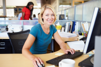 Mujer rubia con camiseta azul trabajando con ordenador en oficina