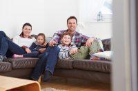 Familia con dos hijos tumbados en un sofá viendo la tv