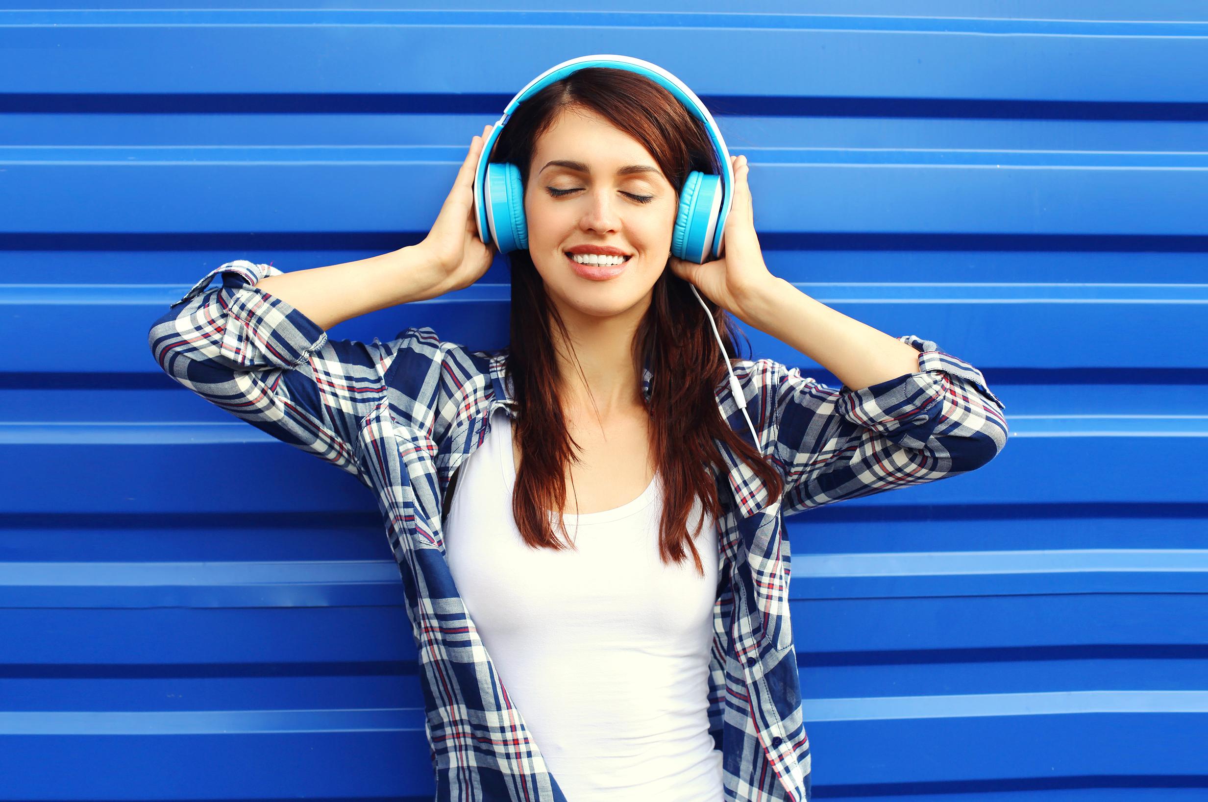 Happy smiling young woman listens and enjoys music in headphones