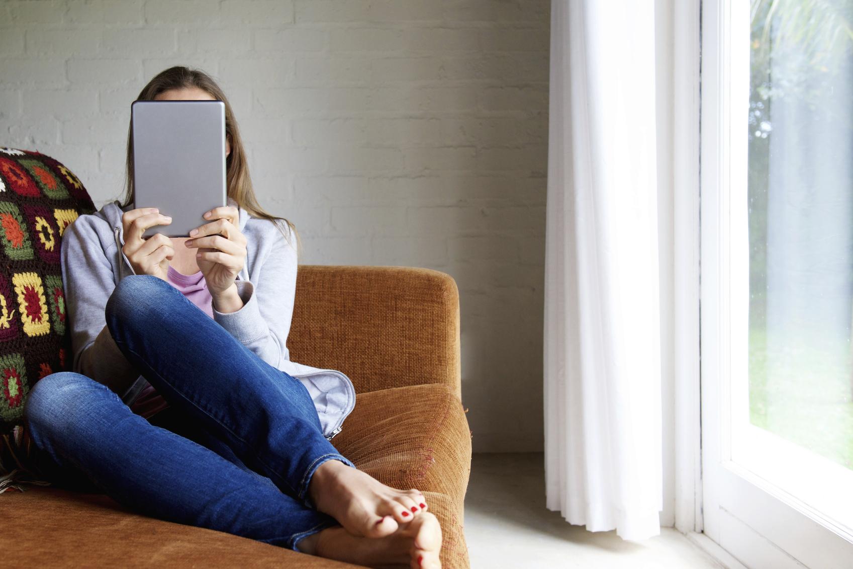 Chica leyendo en una tablet sentada en un sofá