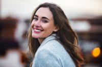 Mujer morena con abrigo gris mira atrás y sonríe