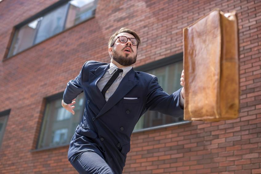 Young businessman with a briefcase and glasses running in a city street on a background of red brick wall. concept of rapid career