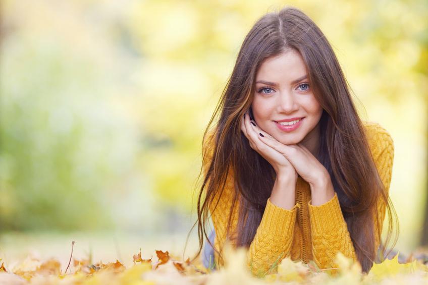 Portrait of a beautiful young brunette woman laying in the autumn park