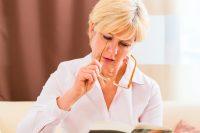 Mujer rubia con pelo corto se pone las gafas para leer