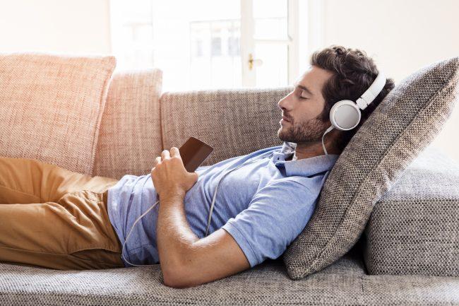 Hombre joven tumbado en un sofá escuchando música