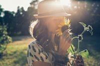 Mujer morena con gorro oliendo una flor