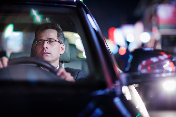 Hombre con gafas conduciendo un coche oscuro