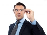 Hombre con traje mirando a través de unas gafas que tiene en la mano