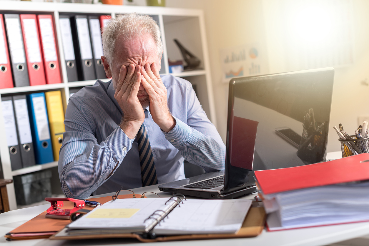 Hombre con corbata se frota los ojos mientras trabaja en la oficina