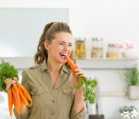 Mujer con camisa verde comiéndose una zanahoria