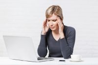 Mujer con jersey gris tiene dolor de cabeza trabajando en ordenador